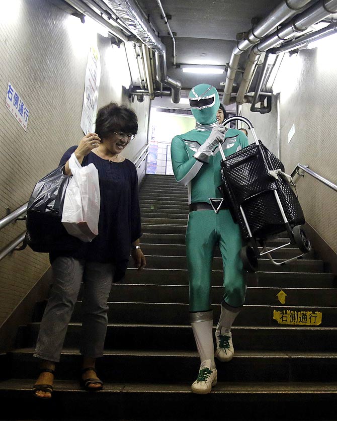 Tadahiro Kanemasu aka the 'Carry-Your-Pram-Ranger' carries a woman's shopping cart at the station in Tokyo.